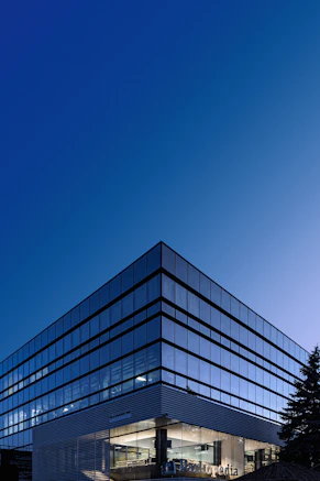A modern glass office building corner against a clear deep blue sky