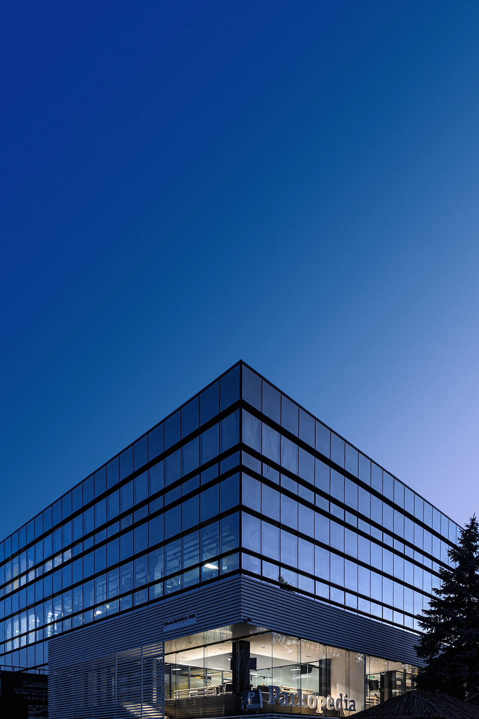 The corner of a glass-fronted office building seen from below against a clear sky