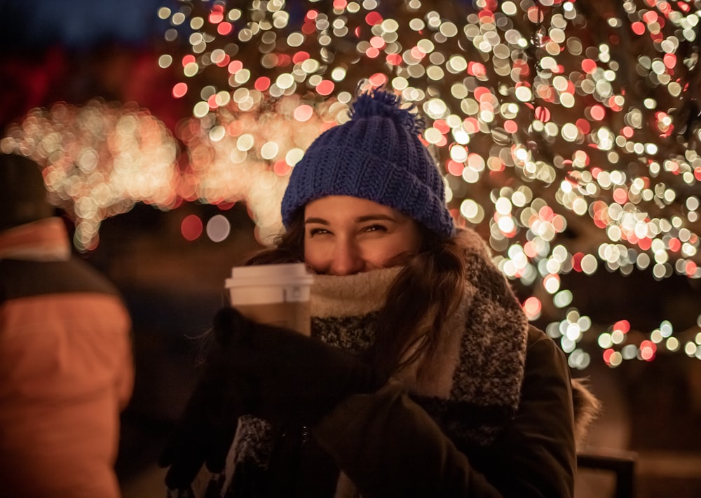 a woman drinking a cup of coffee in front of a christmas tree