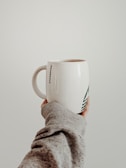 A close-up of a hand holding a mug with a playful, custom logo design.