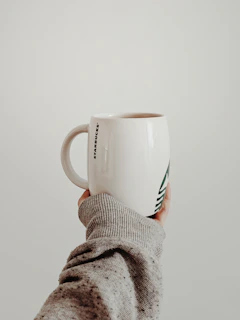 A steaming mug with a bold design, held by hands wrapped in a warm hoodie.