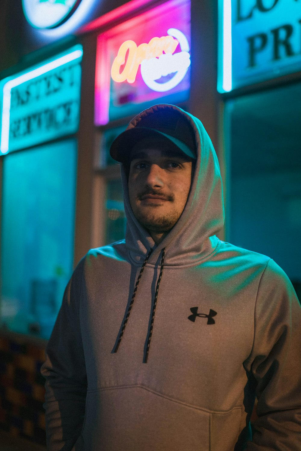 selective focus photography of man wearing Under Amour hoodie in front of building at night