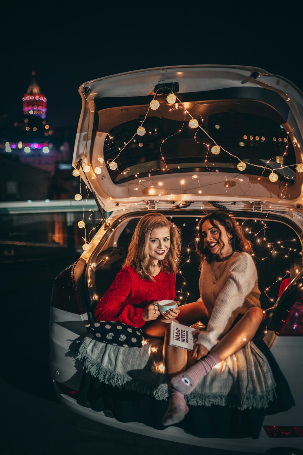 two women sitting on vehicle trunk