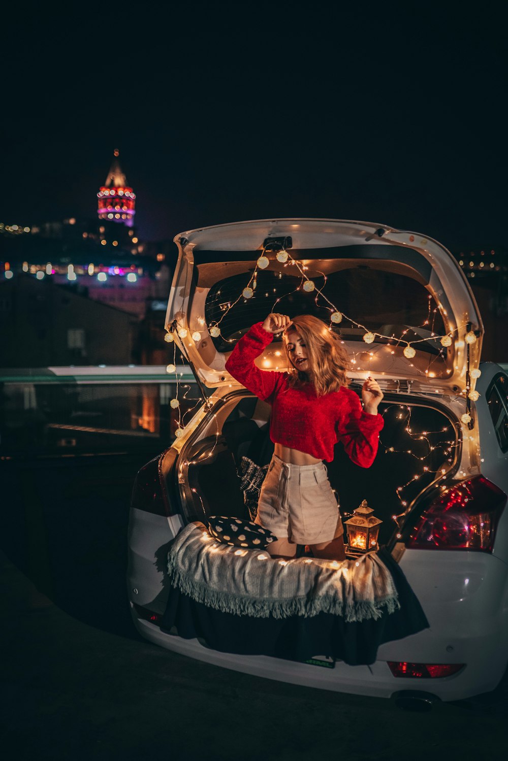 woman kneeling on car trunk with string lights