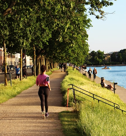 A smiling person jogging along a tree-lined path, embodying active and healthy living.