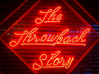 Bright red neon lights spell out 'The Throwback Story' on a background of wooden slats with a geometric pattern. The glow of the neon light creates a striking visual contrast against the dark background.
