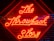 Bright red neon lights spell out 'The Throwback Story' on a background of wooden slats with a geometric pattern. The glow of the neon light creates a striking visual contrast against the dark background.
