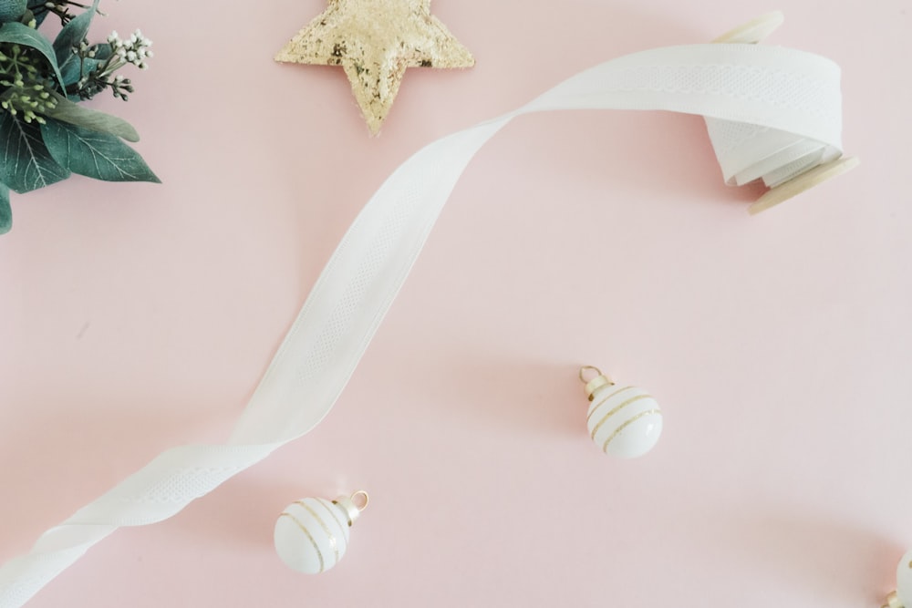 a white ribbon and some ornaments on a pink surface