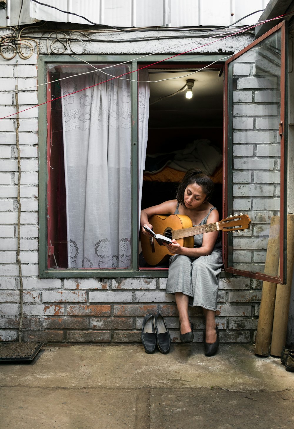 woman sitting on window while playing a guitar