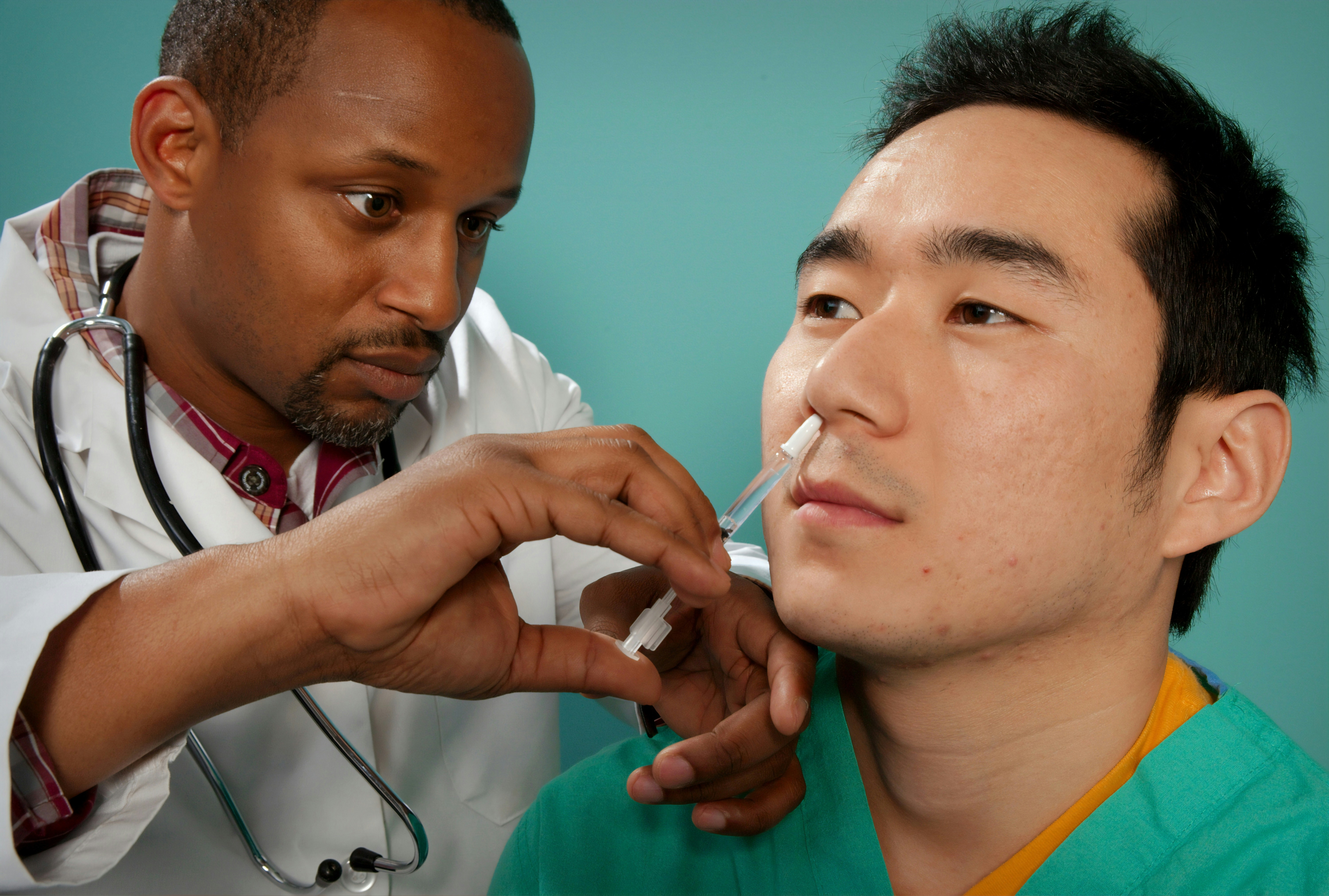 This 2009 image depicts a healthcare practitioner as he was administering the H1N1 live attenuated intranasal vaccine (LAIV) to an Asian man. Using a small syringe, he was delivering the vaccine mist into the man’s right nostril.