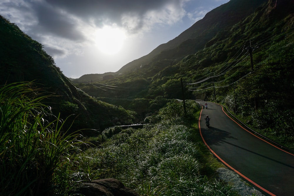 black road between mountain and trees during daytime