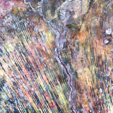 Aerial photograph with a blend of vivid and earthy colors featuring linear patterns that resemble geological formations or agricultural fields. Curved lines and textures suggest natural processes or topographical features.
