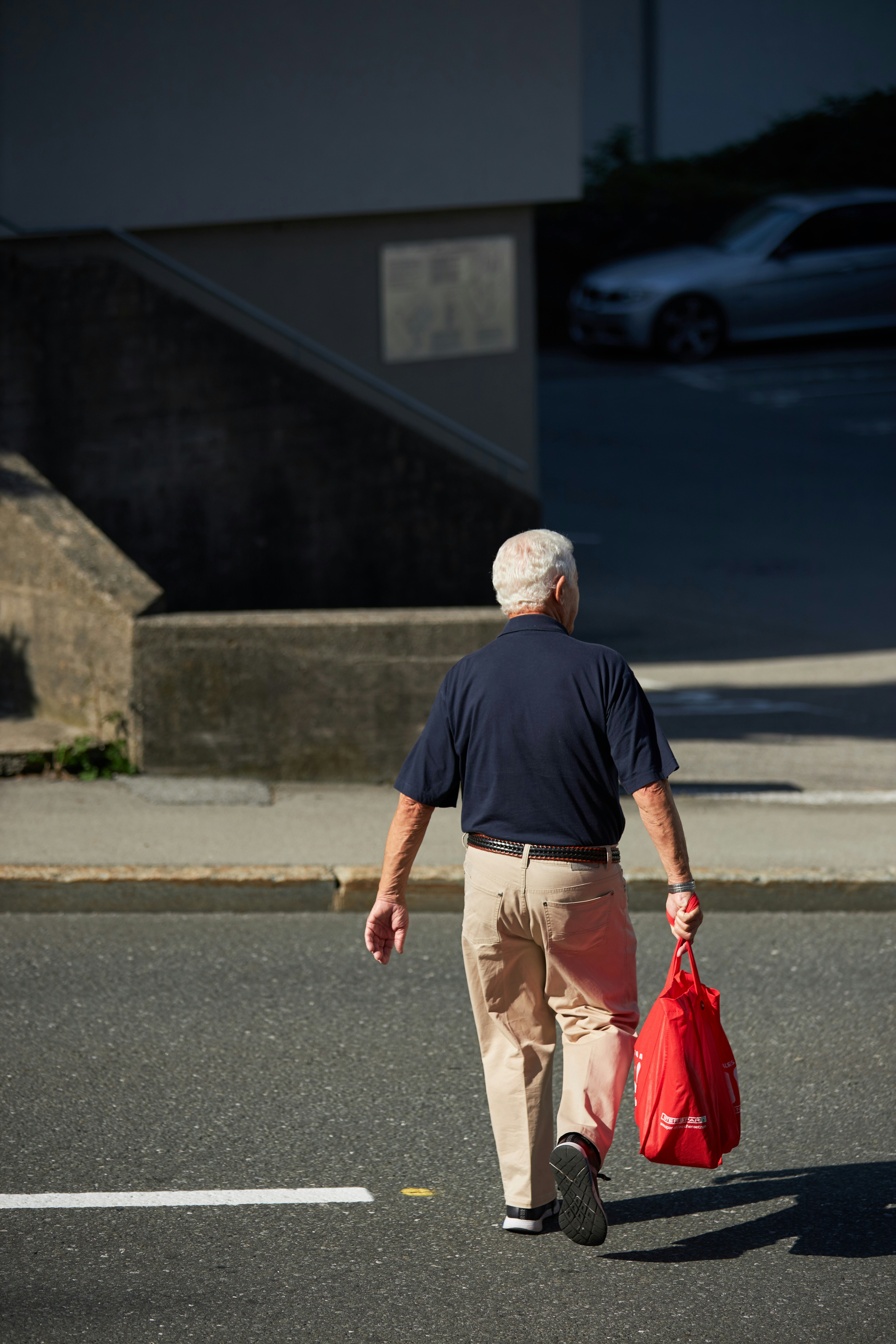 old man, walking, carry, bag, red bag, crossing street, white hair