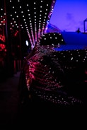Close-up of a sleek luxury car reflecting neon magenta and electric green lights.