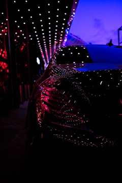 Close-up of a sleek luxury car reflecting neon magenta and electric green lights.