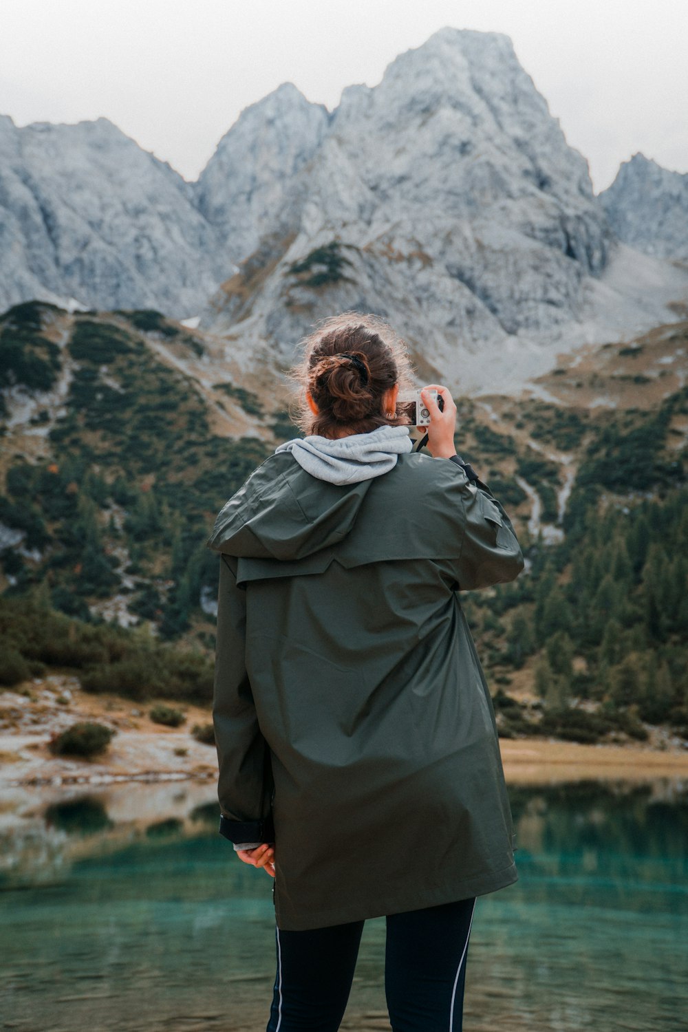 person wearing hooded jacket taking photo of body of water while standing