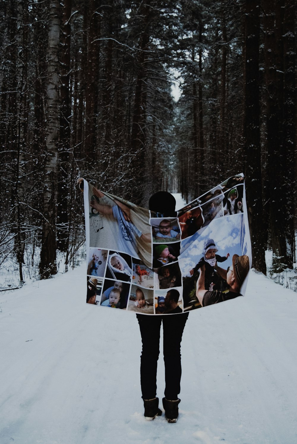 person holding tarpaulin while standing on snowy field surrounded with green trees