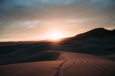 A dramatic desert sunset with silhouettes of quad bikes and Bedouin tents against a glowing orange sky.