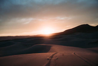 A dramatic sunset over the vast Sahara Desert with rolling sand dunes.