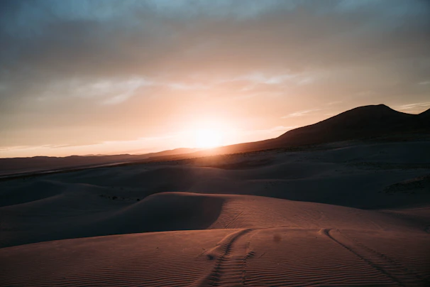 A dramatic sunset over the vast Sahara Desert with rolling sand dunes.