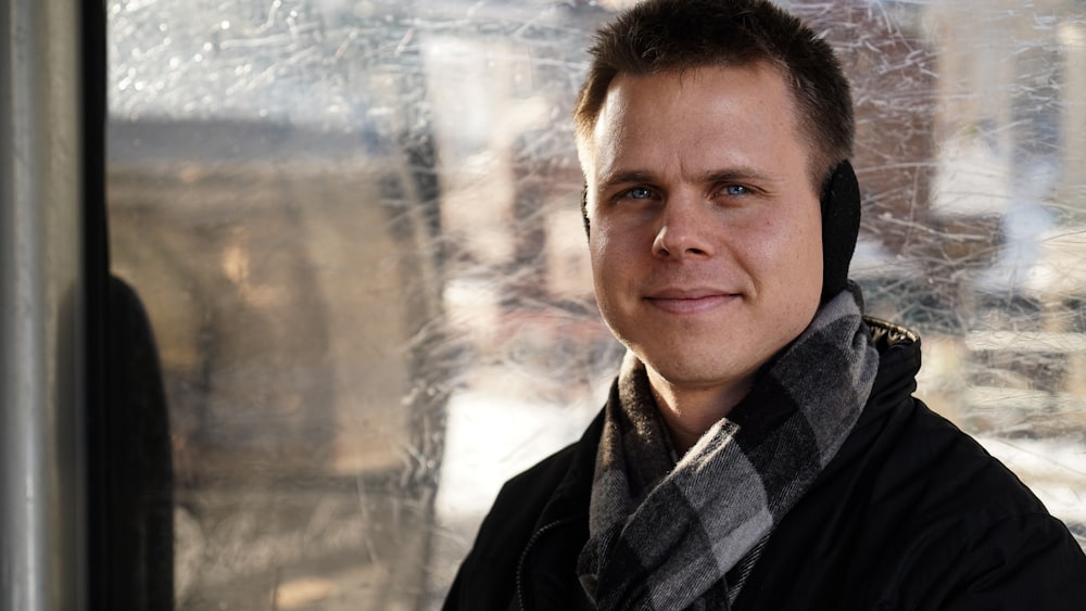 man wearing black jacket and black and gray scarf smiling