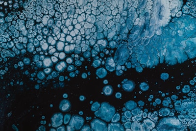 Intricate patterns of blue and white cells create an abstract, organic design. The upper portion has a concentration of cell-like structures which gradually become sparse towards the bottom.
