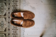 Neutral-toned leather loafers placed on a soft brown rug beside a steaming cup of coffee.