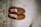 A pair of brown suede loafers is neatly placed on a wooden floor next to a patterned rug. The shoes appear to be well-crafted, with stitching details visible along the edges. The rug features intricate geometric patterns in shades of beige, brown, and black.