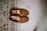 A pair of brown suede loafers is neatly placed on a wooden floor next to a patterned rug. The shoes appear to be well-crafted, with stitching details visible along the edges. The rug features intricate geometric patterns in shades of beige, brown, and black.