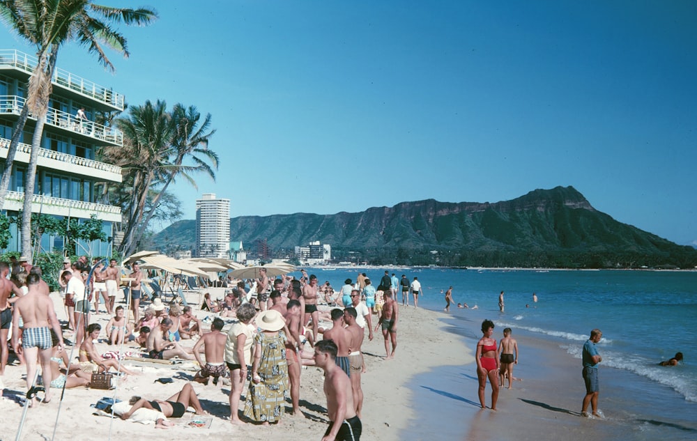 people on beach near seaside resort viewing mountain during daytime