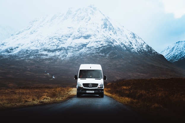 A white camper in a rainy landscape with a wet snowy mountain in the backdrop