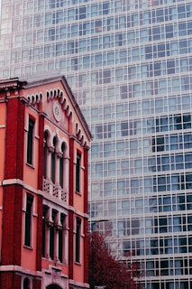 A red-brick historic building stands adjacent to a modern glass skyscraper. The older structure displays ornate architectural details, including arches and decorative trim, contrasting with the minimalist grid pattern of the glass building.