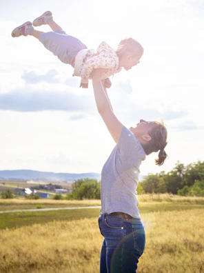 A father lifting his toddler high in the air, both smiling under a clear blue sky.