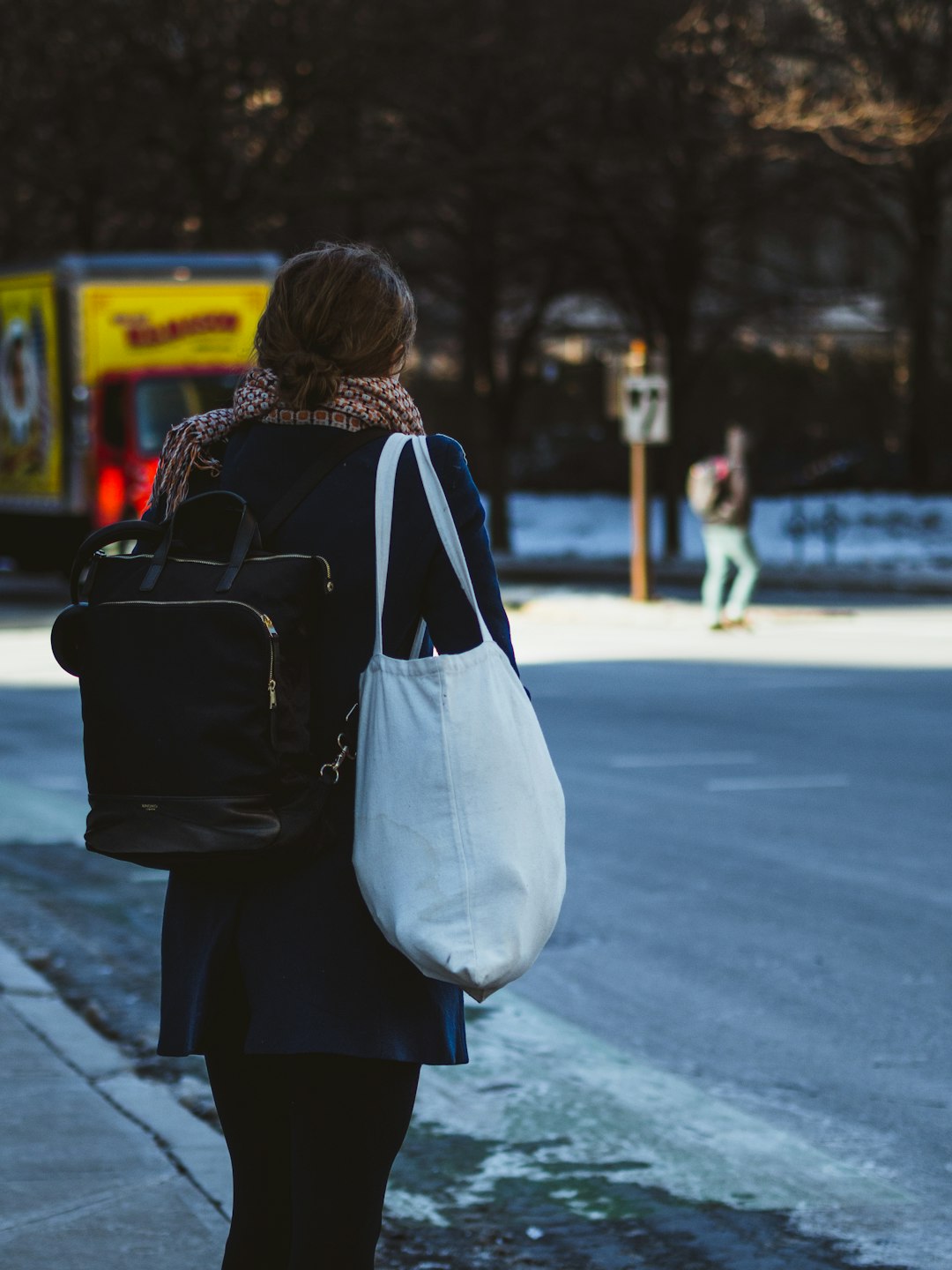 woman wearing black coat with backpack and white shoulder bag standing on road