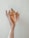 A hand holding a large, textured conch shell against a pale background. The shell has a rough, spiky outer surface and a smooth interior with shades of tan and peach. The fingers are gently wrapped around the shell, showcasing the intricate details and natural beauty of the shell.