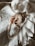 A necklace of pearls is artfully draped over a seashell resting on a textured, white, embroidered fabric. The scene is softly lit, creating gentle shadows and highlights that emphasize the elegance and simplicity of the composition.