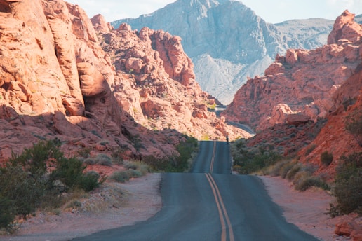 A winding desert road cutting through red rock formations under a warm sunset sky.