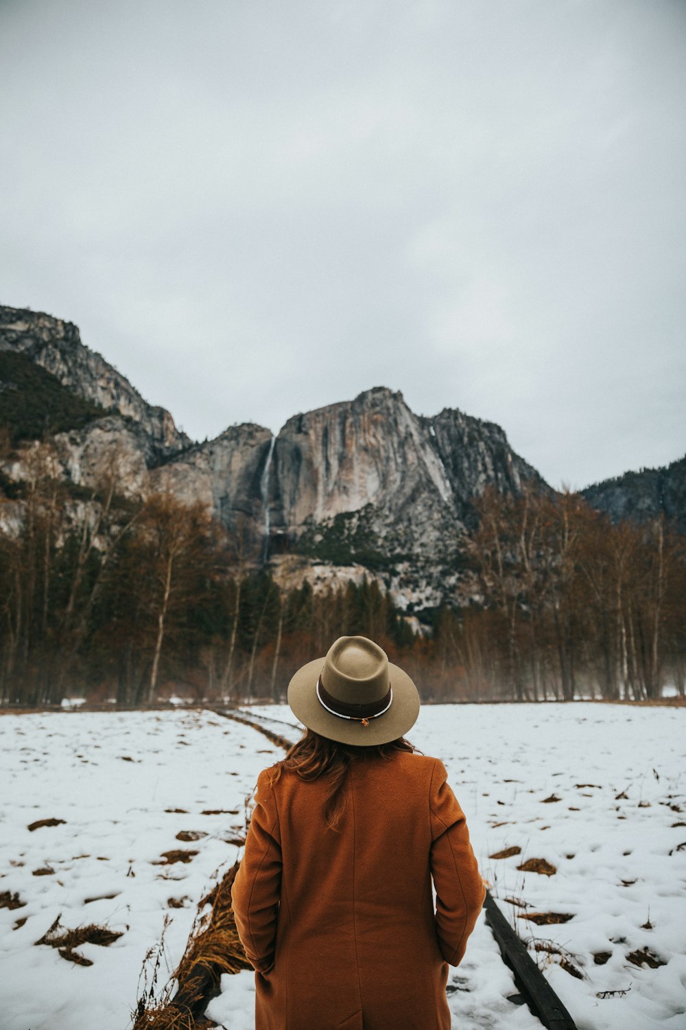 Femme portant un trench-coat marron et un chapeau beige marchant sur une surface glacée