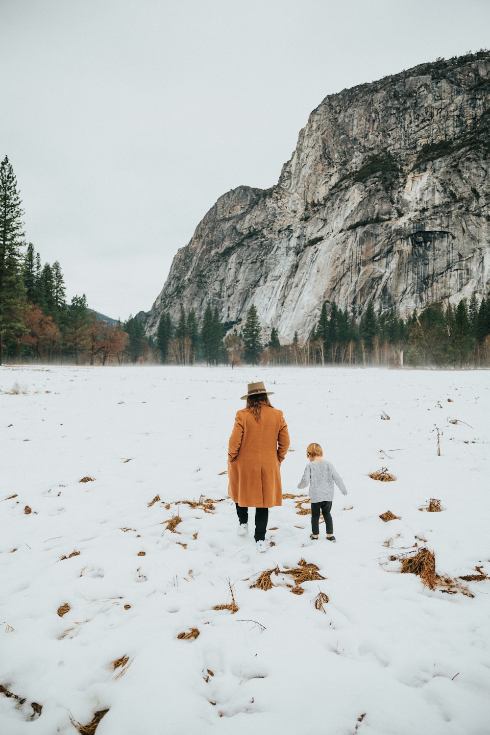 woman and toddler walking on snow-covered field during daytime