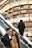 Two people are on an escalator inside a bookstore. They appear to be engaged with something on a smartphone, with a backdrop of multiple shelves filled with books. Another person is ascending on the parallel escalator.