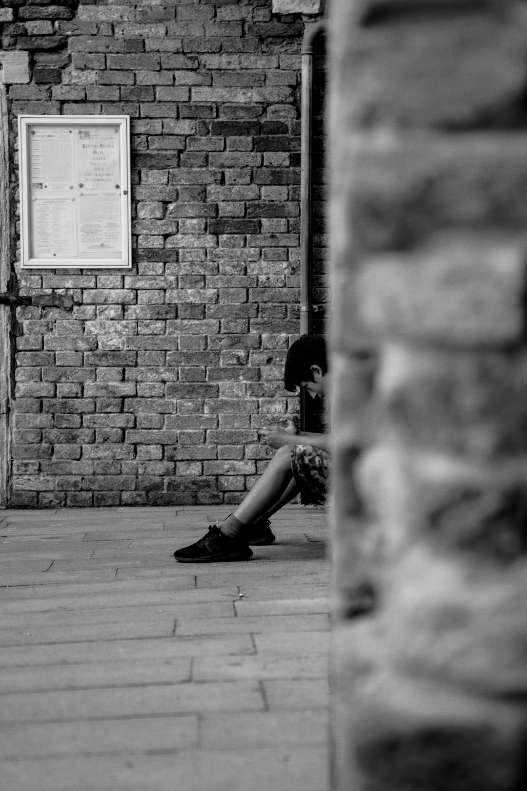 grayscale photo of person sits beside wall