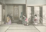 Three women dressed in traditional kimono are engaged in a cultural activity inside a room with tatami flooring. One is arranging flowers, while the other two appear to be observing or participating in a traditional Japanese tea ceremony. The room features classical Japanese art and decorations, including a painted screen and hanging scroll.