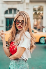 Casual chic look with high-waisted jeans, a tucked-in white blouse, and bold red lipstick on a sunny city sidewalk.