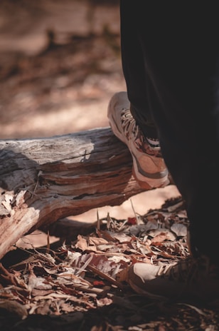 Close-up of trekking boots walking on a forest trail covered with autumn leaves.