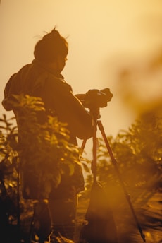 A thoughtful filmmaker capturing nature’s subtle wonders with high-end camera gear in golden light.