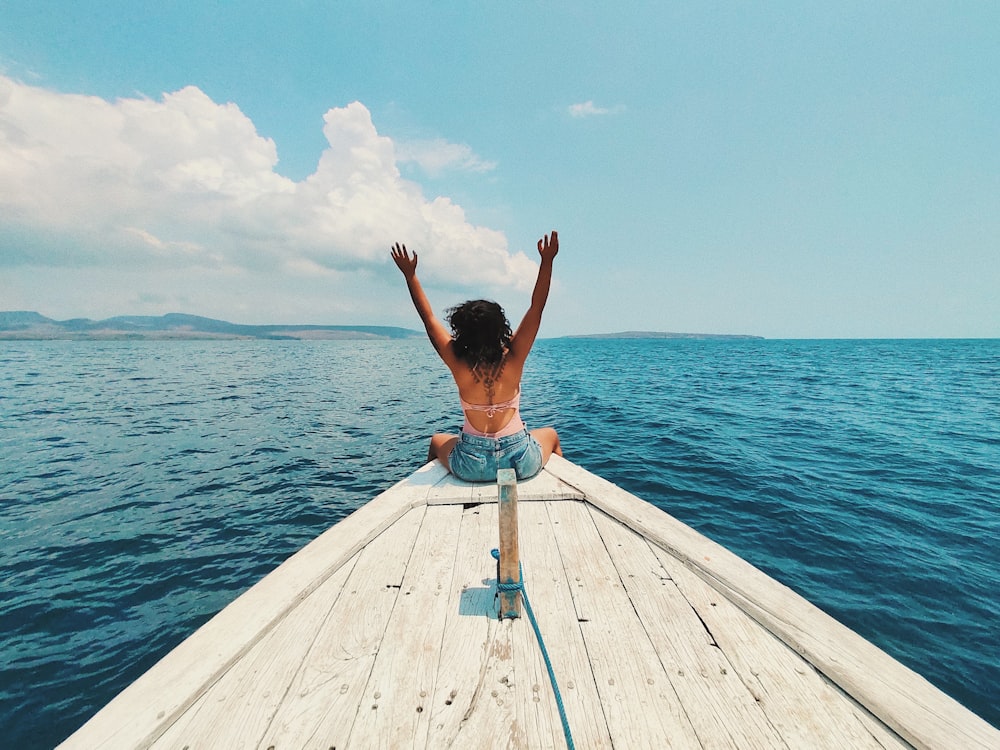 woman wearing blue denim short-shorts sitting on boat raising hands