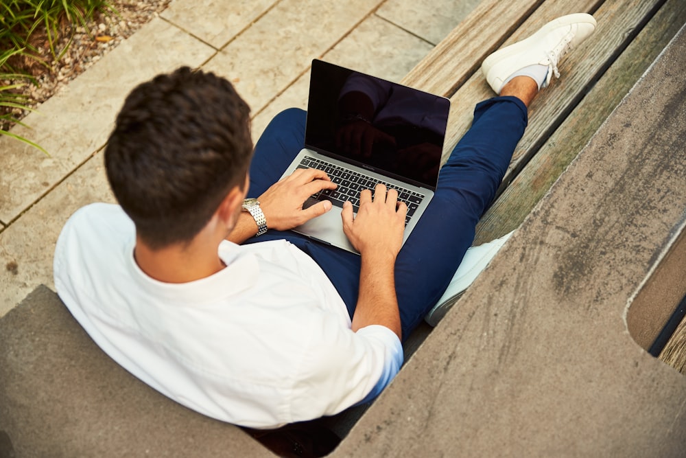 man wearing white sweatshirt using laptop computer sitting on sofa chair