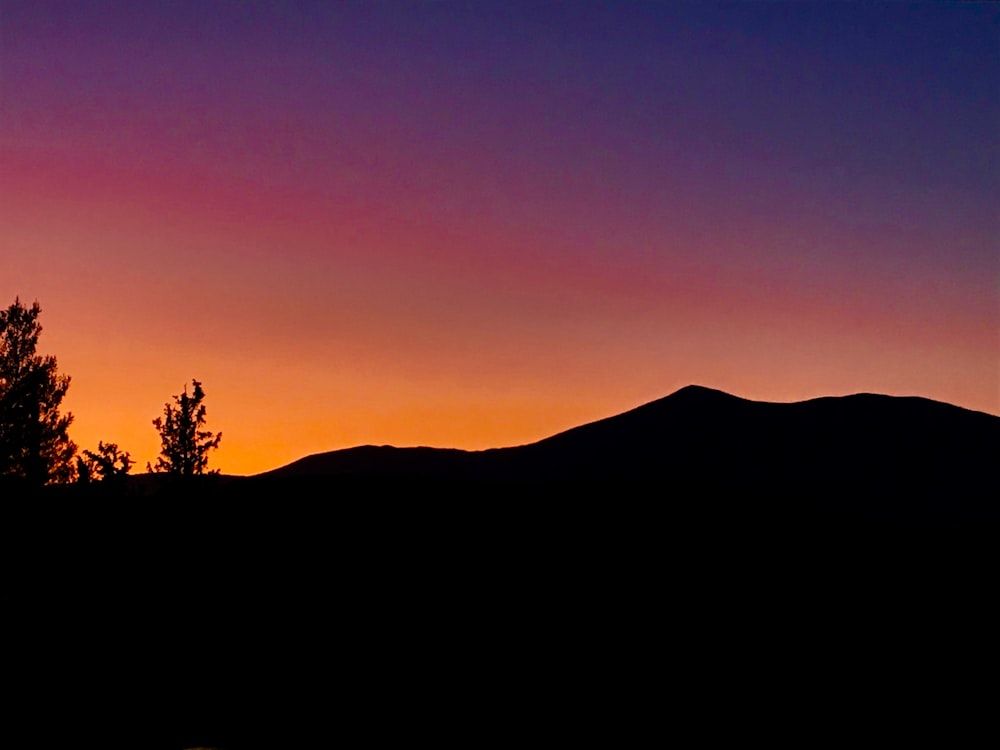 silhouette photography of a mountain under a purple sky during golden hour