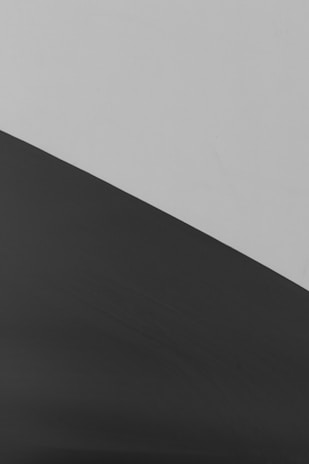 A minimalist composition featuring a diagonal line separating two contrasting areas. The upper section is a smooth, light gray, while the lower section is a dark, almost black shade with subtle texture.