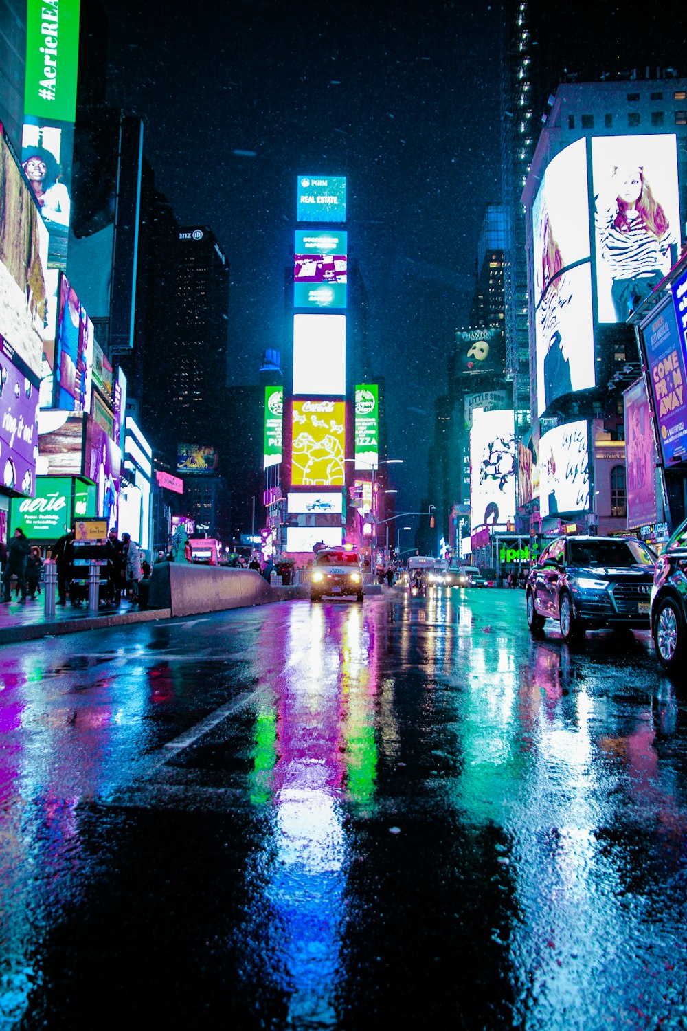 people walking on pathway near buildings and different vehicles on road during night time